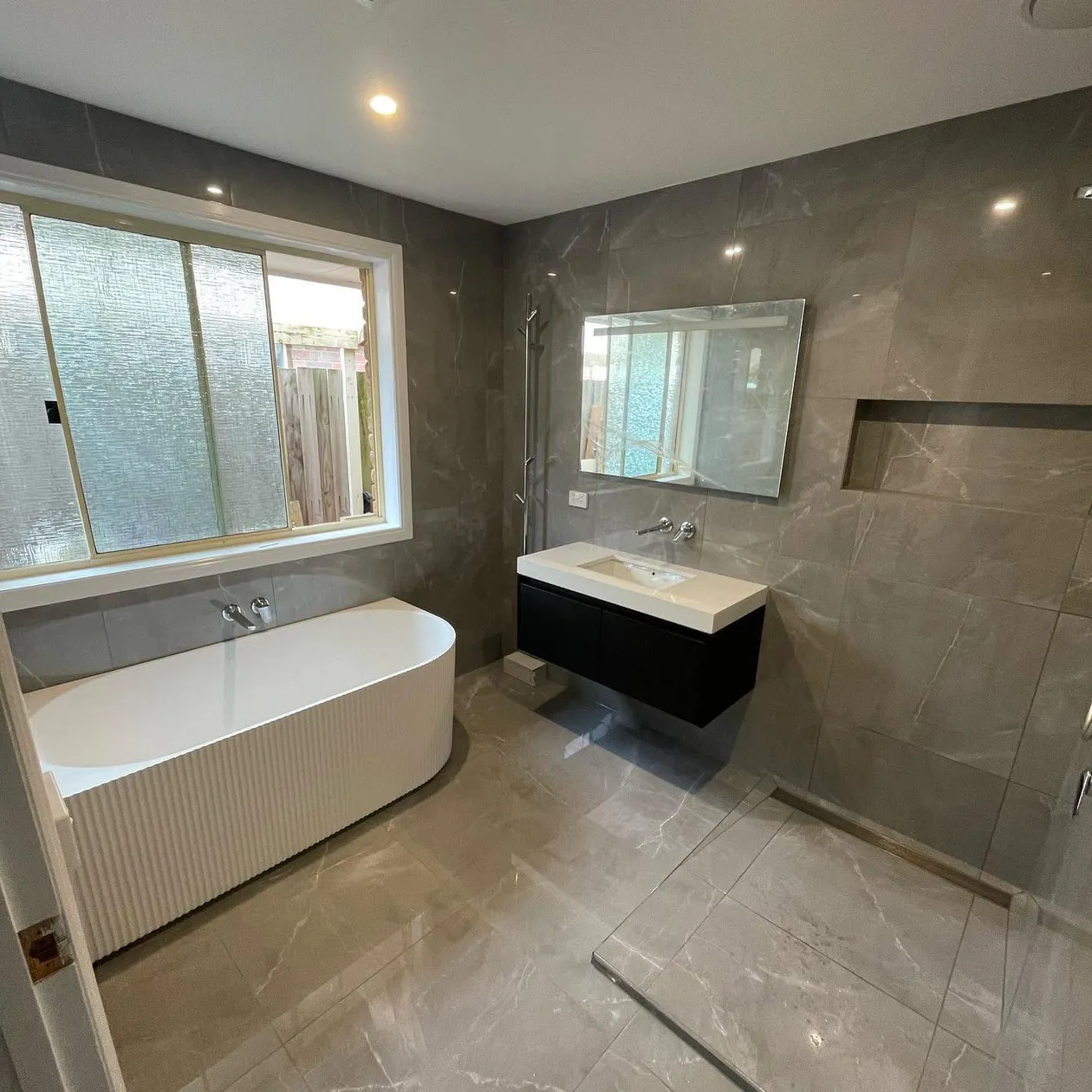 Completed bathroom renovation with a freestanding bath and stone-look tiling