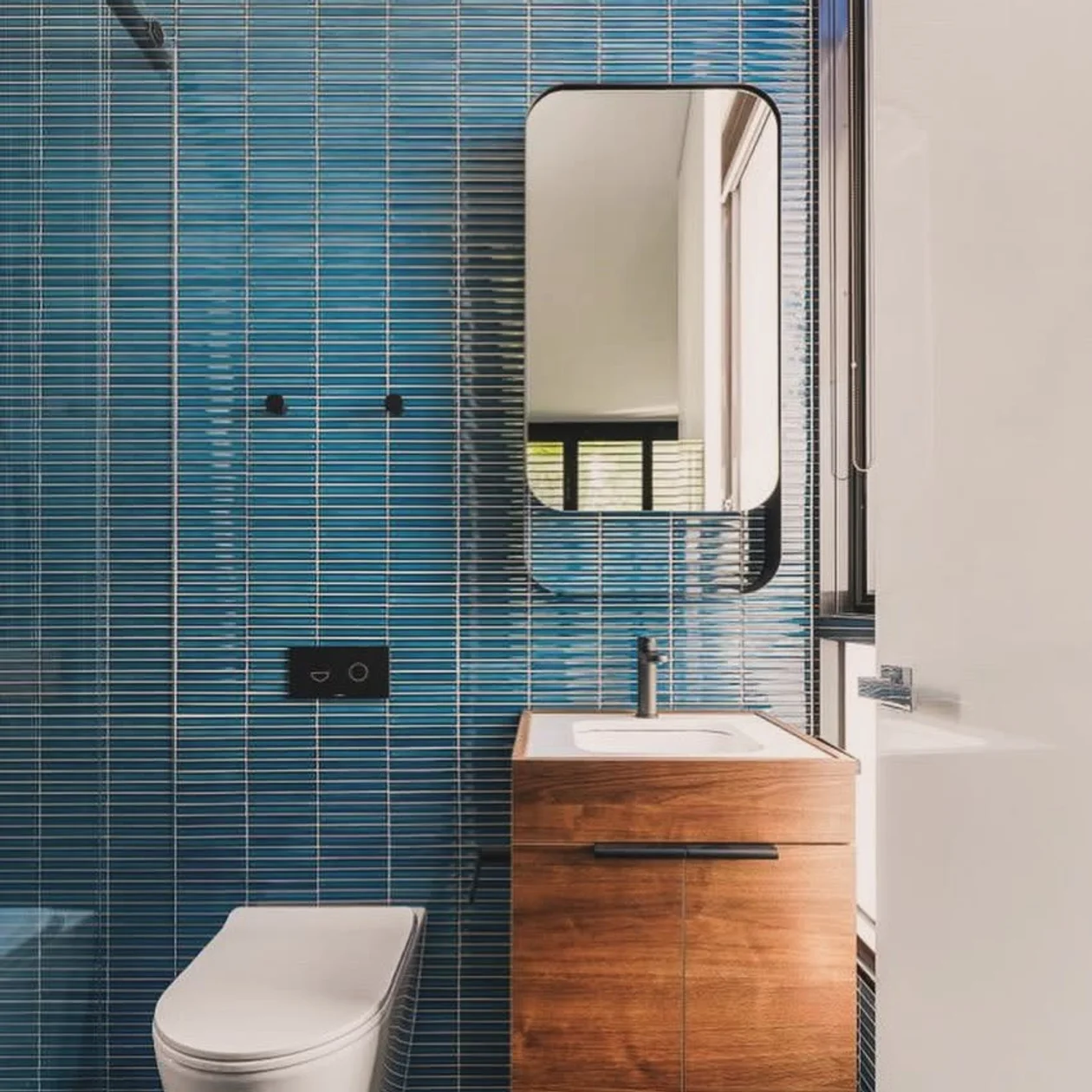 Completed bathroom with vertical blue tiling and a timber vanity