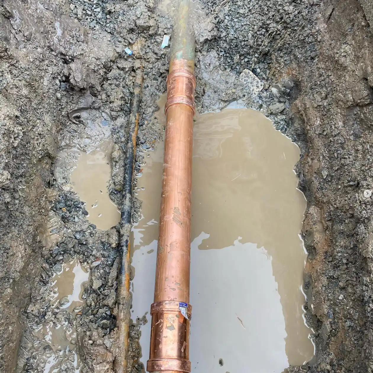 Copper water service pipe exposed in a wet trench during a repair