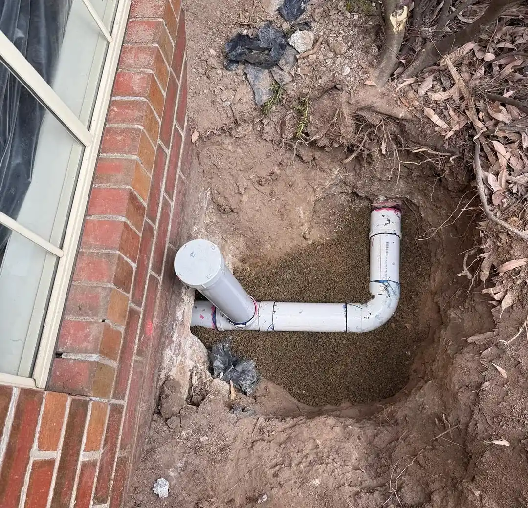 New PVC drainage pipe laid in a trench beside a brick wall